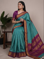 Load image into Gallery viewer, Woman wearing a turquoise saree with a purple blouse, posing in front of plants.