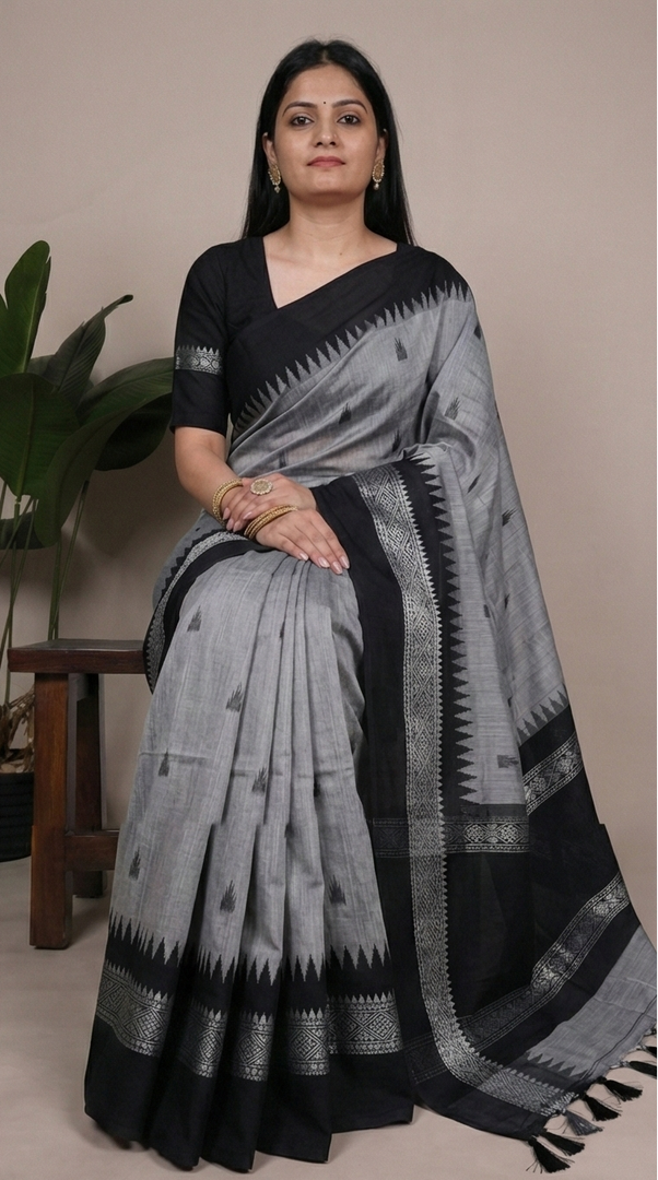 Woman wearing a gray and black saree with a plant in the background