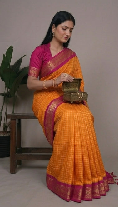 Woman wearing an orange saree with a pink border, sitting and posing against a neutral background.