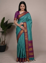 Load image into Gallery viewer, Woman wearing a turquoise saree with a purple blouse, posing in front of plants.