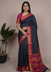 Woman wearing a blue saree with pink and red border, sitting and posing against a neutral background.