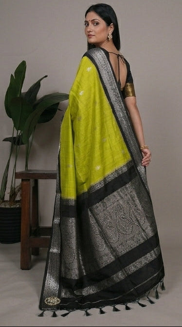 Woman wearing a green and black saree with a plant in the background