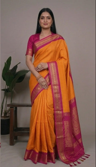 Woman wearing an orange saree with a pink border, sitting and posing against a neutral background.