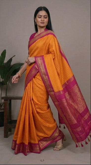 Woman wearing an orange saree with a pink border, sitting and posing against a neutral background.