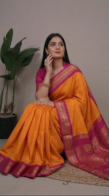 Woman wearing an orange saree with a pink border, sitting and posing against a neutral background.